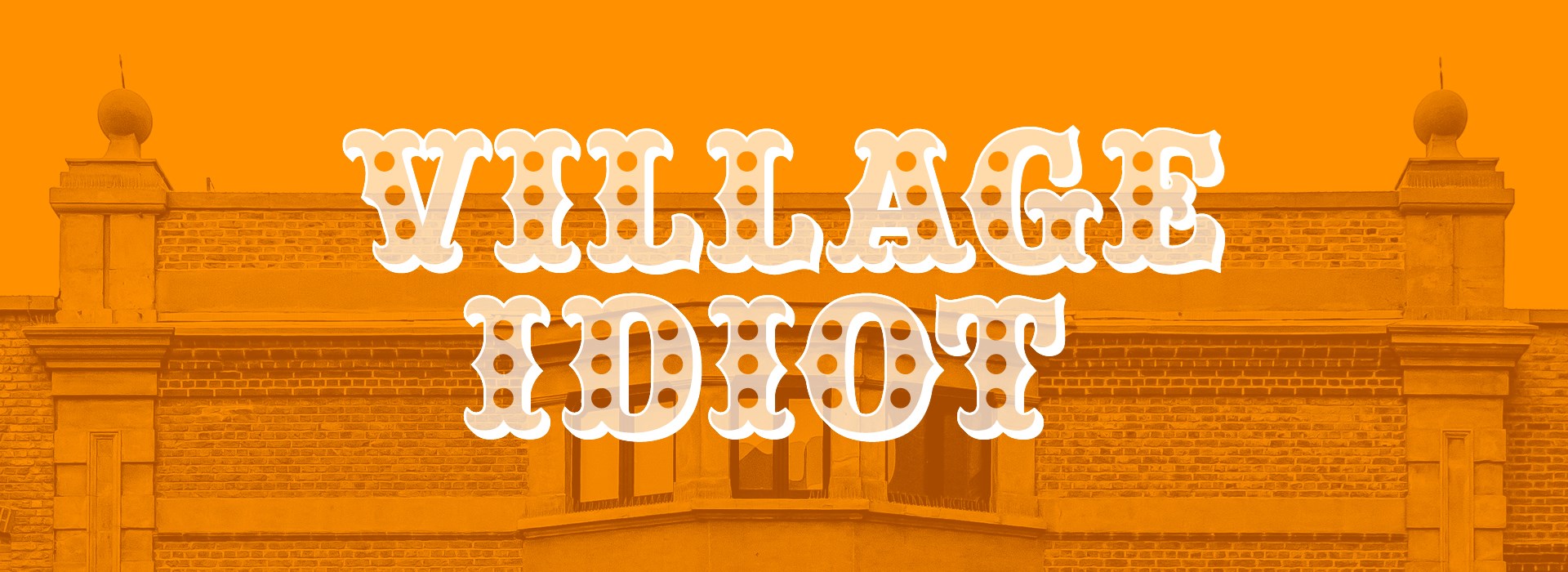A photo of a grand building, like a town hall, is bathed beneath an orange colour, the words 'Village Idiot' written over the top in an old-fashioned white font.
