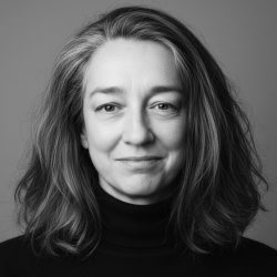 A balck and white headshot of zanna Hornby, she has a long brown bob, and is smiling into the lens.
