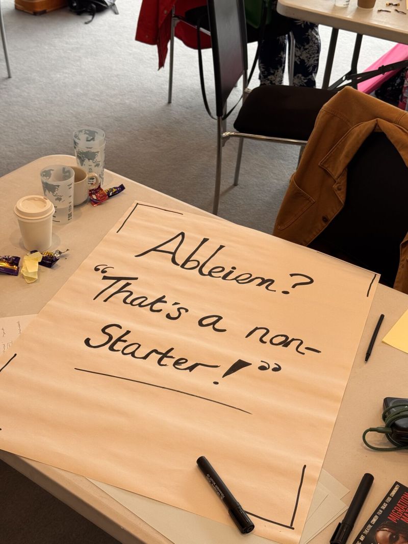 Photo of a large flip chart sheet lying on a table with lots of pens and mugs and stationary around it. The flip chart page as Ableism? Thats a non starter written on it